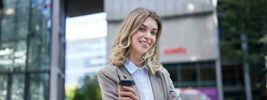 Professional woman standing with coffee in a busy street, smiling at camera photo