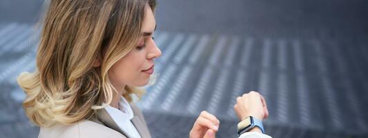 Close up portrait of business woman looking at her wrist digital watch, reading message, using app, standing outdoors in city center photo