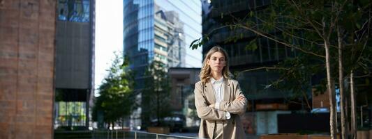 confidente mujer de negocios en traje, sostiene manos cruzado en pecho, soportes en poder actitud en calle foto