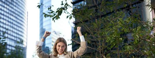 Saleswoman expresses joy and happiness. Businesswoman triumphing on street, raising hands up, celebrating victory, smiling pleased photo