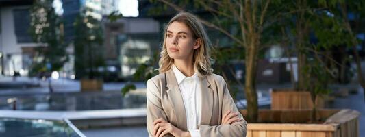 Close up portrait of confident and successful businesswoman in suit, cross arms on chest, standing in power pose on street near office building photo