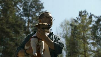 Man holds dog in arms in park. Stock footage. Handsome man with dog in arms walks in forest in summer. Man with dog on sunny summer day photo