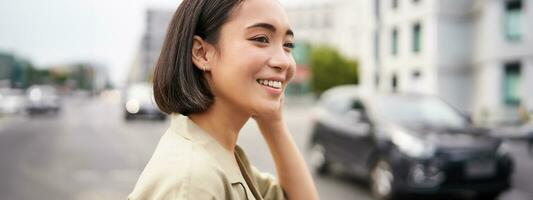 Close up portrait of beautiful young woman, asian girl stands outdoors on street, smiling happy photo