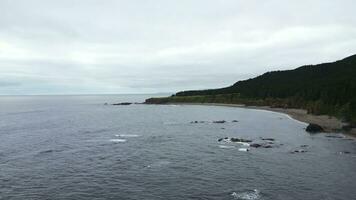 Green mountains with rocky reefs in cloudy weather. Clip. Landscape of mountain coast with green forest on cloudy day. Beautiful northern coast with green forest and blue sea waves photo