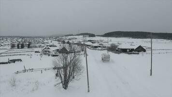 Top view of small village in winter. Clip. Truck drives through small old village in winter. Winter landscape with old rare village on cloudy day photo