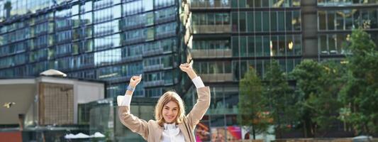 Corporate woman celebrating her victory outside on street. Happy businesswoman raising hands up and triumphing from excitement photo