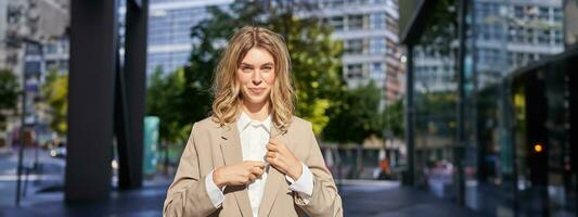 Close up portrait of confident business woman, corporate lady in beige suit, looking determined and ready, standing outside office building on street photo