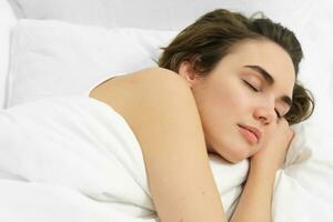 Woman lying asleep in her bed, eyes closed, face is calm and relaxed, hugging soft, comfortable pillow photo