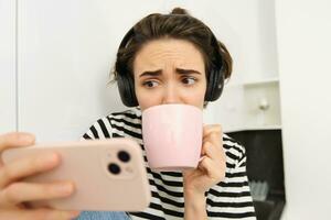 Portrait of woman with sad and worried face, watching intense tv series on smartphone app, drinking tea and staring at mobile phone screen photo