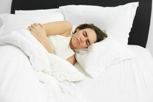 Portrait of woman feeling unwell, lying in bed and touching her belly, frowning from painful menstrual cramps, having period pain, resting in bedroom photo