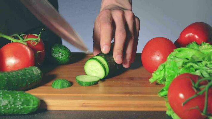Man Slicing Cucumber While Woman Steals Another Vegetables From the Table. Strong Impatience for Eating. Family Funny Cooking Concept. CloseUp Shot Static View