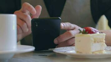 joven hombre en café utilizando un teléfono inteligente cliente en un negro camisa tiene un café descanso en el tiempo de día video