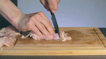 capocuoco nel nero uniforme è taglio pollo filetto. macellaio è preparazione cibo ingredienti per cucinando lento movimento. statico tiro video