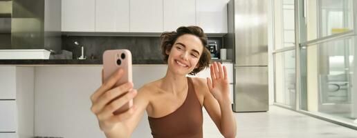 imagen de joven aptitud niña bloguero, registros su rutina de ejercicio a hogar, chats en línea mientras haciendo yoga en brillante habitación. mujer con teléfono inteligente, unión remoto yoga formación vía móvil teléfono foto