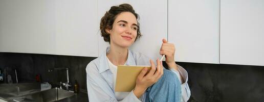 Indoor shot of young woman relaxing at home, reading journal, studying in comfort, spending time inside her house photo