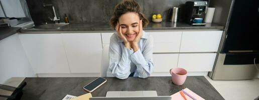 Beautiful self-employed girl works from home. Young woman online studying, watching course on website, looking at laptop screen photo