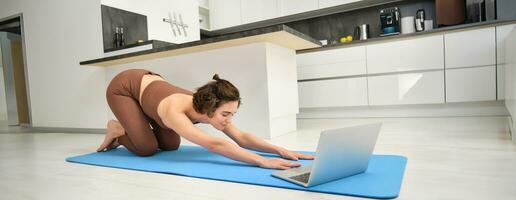 Image of girl athlete, sportswoman practice yoga, follow online video class on laptop, watching training workout instructions on computer, exercising from home photo