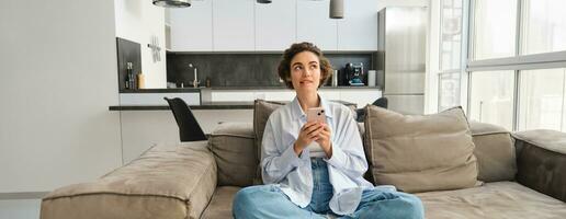 Portrait of smiling woman chats on smartphone app, sits at home on sofa and uses mobile phone application photo