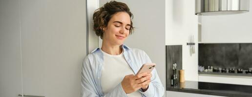 Portrait of brunette woman with smartphone, sending message, checking her mobile application, ordering delivery to home photo