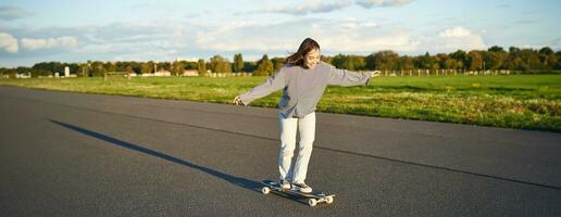 aficiones y estilo de vida. joven mujer montando patineta. patinador niña disfrutando crucero en longboard en soleado día al aire libre foto