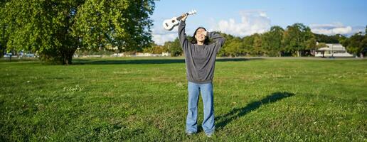 contento asiático chica, músico con ukelele, sensación despreocupado, disfrutando libertad y Fresco aire al aire libre, jugando musical instrumento foto