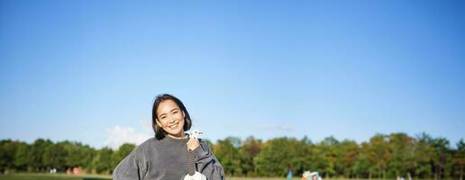 Beautiful girl poses with her ukulele, shows musical instruments, stands on green field on sunny day photo