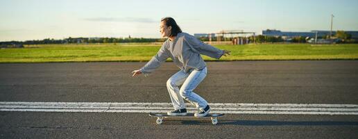 Happy skater girl riding her skateboard and having fun on empty street. Smiling woman enjoying cruiser ride on sunny road photo