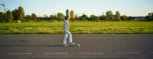 Beautiful asian skater girl riding her longboard on sunny empty road. Young woman enjoying her skate ride smiling and laughing photo