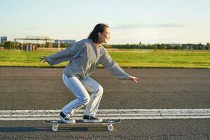 Happy skater girl riding her skateboard and having fun on empty street. Smiling woman enjoying cruiser ride on sunny road photo