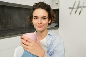 Image of young adult woman with cup of coffee. Girl relaxed at home, drinks tea, has a break from work photo