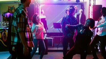 Cheerful adults dancing at disco party, having fun at social gathering on dance floor. Modern funky people showing cool dance moves on live music at nightclub, entertainment. Handheld shot. photo