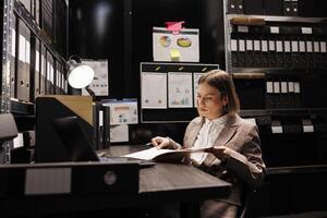 Private detective holding investigations files, analyzing crime scene evidence trying to catch mysterious suspect. Caucasian investigator checking victim report, working late at night in arhive room photo