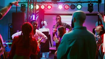 multitud de amigos teniendo divertido a fiesta en danza piso y escenario, haciendo frio danza se mueve a disco celebracion evento. joven personas bailando en moderno electrónico música, deslumbramientos. Mano disparo. foto