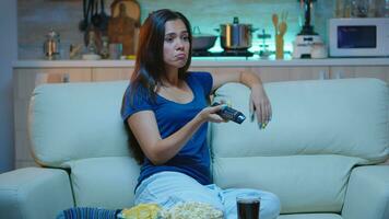 Bored woman resting watching tv in living room sitting on couch. Tired from work, home alone late at night lady relaxing on sofa in front television holding remote control choosing channel with movie photo