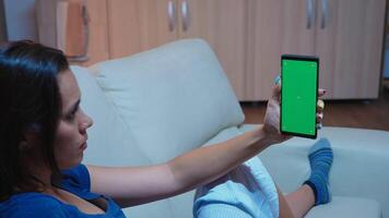 Lady reading on smartphone monitor with green screen lying on sofa in living room. Woman holding a mobile phone with mockup template chroma key isolated cell phone display using techology internet photo