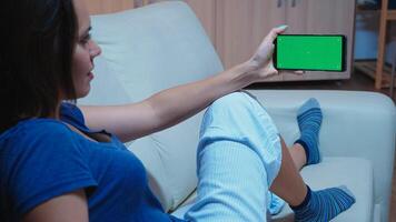 Caucasian woman in pijamas looking at smart phone with green screen. Lady holding a mobile phone with mockup template chroma key isolated cell phone display using techology internet photo
