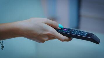 Television remote control in the hands of woman pointing to TV and changing channels. Close up of woman holding controller and pressing the button sitting on couch in front of television. photo