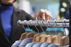 Clothing store assistant hand counting apparel on rack, checking and adjusting merchandise in stock closeup. Shopping center showroom employee arm managing garment inventory photo