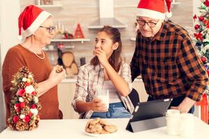 Multi generation family enjoying dessert on christmas day. Happy child wearing santa hat eating delicious cookies from grandparent while celebrating winter holidays with them. photo