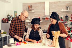 Grandparent and granddaughter on christmas day making traditional dessert. Happy cheerful joyfull teenage girl helping senior woman preparing sweet cookies to celebrate winter holidays. photo