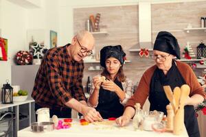 Granddaughter on christmas day making dessert for santa wearing apron. Happy cheerful joyfull teenage girl helping senior woman preparing sweet cookies to celebrate winter holidays. photo