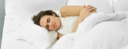 joven mujer acostado en cama con estómago dolor, tiene doloroso calambre, menstrual dolor foto