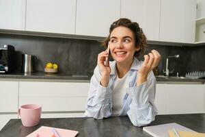 Cellular technology and people. Smiling brunette woman sits at home in kitchen, talks on mobile phone photo