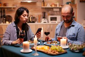 Pareja comida juntos utilizando teléfono inteligente en cocina. adultos sentado a el mesa ,hojeada, buscando, utilizando teléfonos inteligentes, Internet, celebrando aniversario. foto