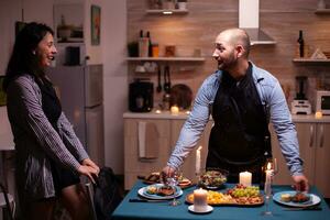 alegre marido sorprendente esposa con cena en comida habitación después ella llega desde trabajar. hombre preparando festivo cena con sano alimento, Cocinando para su mujer un romántico cena, foto