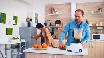 Couple mixing various fruits for nutritious and healthy smoothie in kitchen. Cheerful family making together organic healthy fresh nutritious tasty juice for breakfast from fresh fruits while on a diet. photo