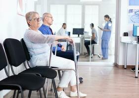 Senior woman with walking frame in hospital waiting room for rehabilitation treatment. Medical staff discussing about patient x-ray. photo