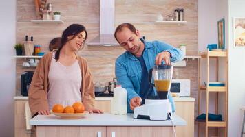 Man pouring milk in blender for fresh and healthy smoothie for him and cheerful wife. Cheerful family making together organic healthy fresh nutritious tasty juice for breakfast from fresh fruits while on a diet. photo