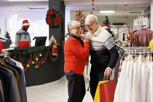 Elderly people doing sweet waltz dance in retail store, showing sincere feelings at mall during seasonal christmas promotions. Romantic man and woman dancing around in shopping center, xmas spirit. photo