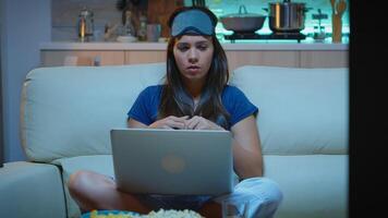 Exhausted person talking on webcam with colleagues using laptop from home sitting on couch. Lady in pijamas with eye mask having video calling on notebook computer at night using internet technology photo